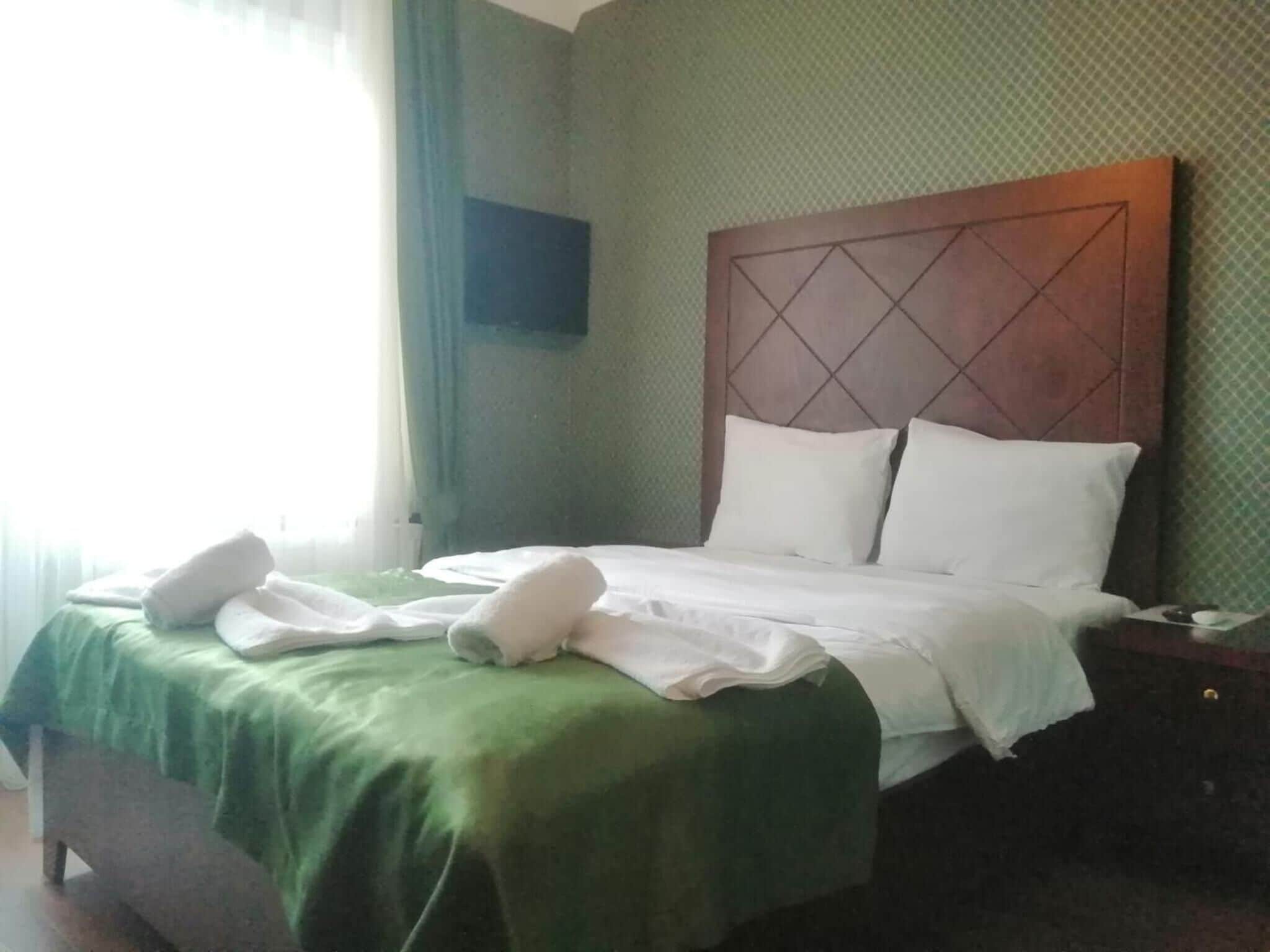 A neatly made bed with white linens and pillows, a green bedspread, and a wooden headboard.