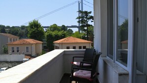 A balcony with a chair and a window overlooking a residential area with houses and a bridge.