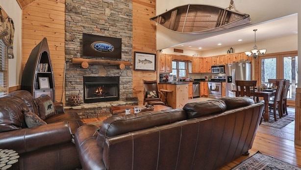 A spacious living area with a stone fireplace, leather sofas, and a kitchen in the background. - Tie One On The River | Ellijay, GA (Ellijay)
