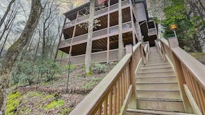 A multi-level wooden cabin with a staircase leading to the entrance, surrounded by trees. - Tie One On The River | Ellijay, GA (Ellijay)