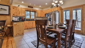A wooden cabin-style kitchen with a dining table, chairs, a refrigerator, and a chandelier. - Tie One On The River | Ellijay, GA (Ellijay)