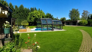 A backyard with a swimming pool, a covered seating area, and a well-maintained lawn.