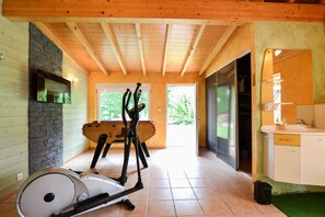 Amplia habitación con techo de madera, pared de piedra, ventana grande, cinta de correr y baño con espejo y lavabo.