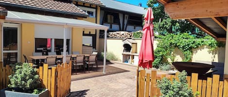 An outdoor patio with wooden furniture, a red umbrella, and a brick floor.