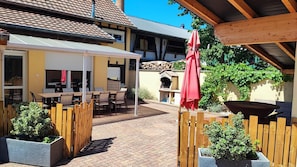 Une terrasse extérieure avec des meubles en bois, un parasol rouge et un sol en briques.