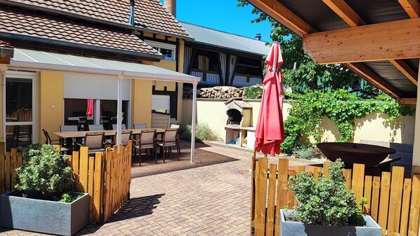 An outdoor patio with wooden furniture, a red umbrella, and a brick floor.