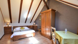 A bedroom with a wooden bed, a wooden wardrobe, a table with a green tablecloth, and a chair.