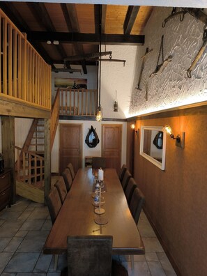 A dining area with a long wooden table, chairs, and a staircase leading to an upper level. - Rural Cottage, indoor swinming pool and spa, playg (Ostheim)