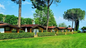 Une rangée de cabanes en bois aux toits rouges, entourées de haies et d’arbres bien entretenus, se dressant sur fond d’un ciel bleu clair.