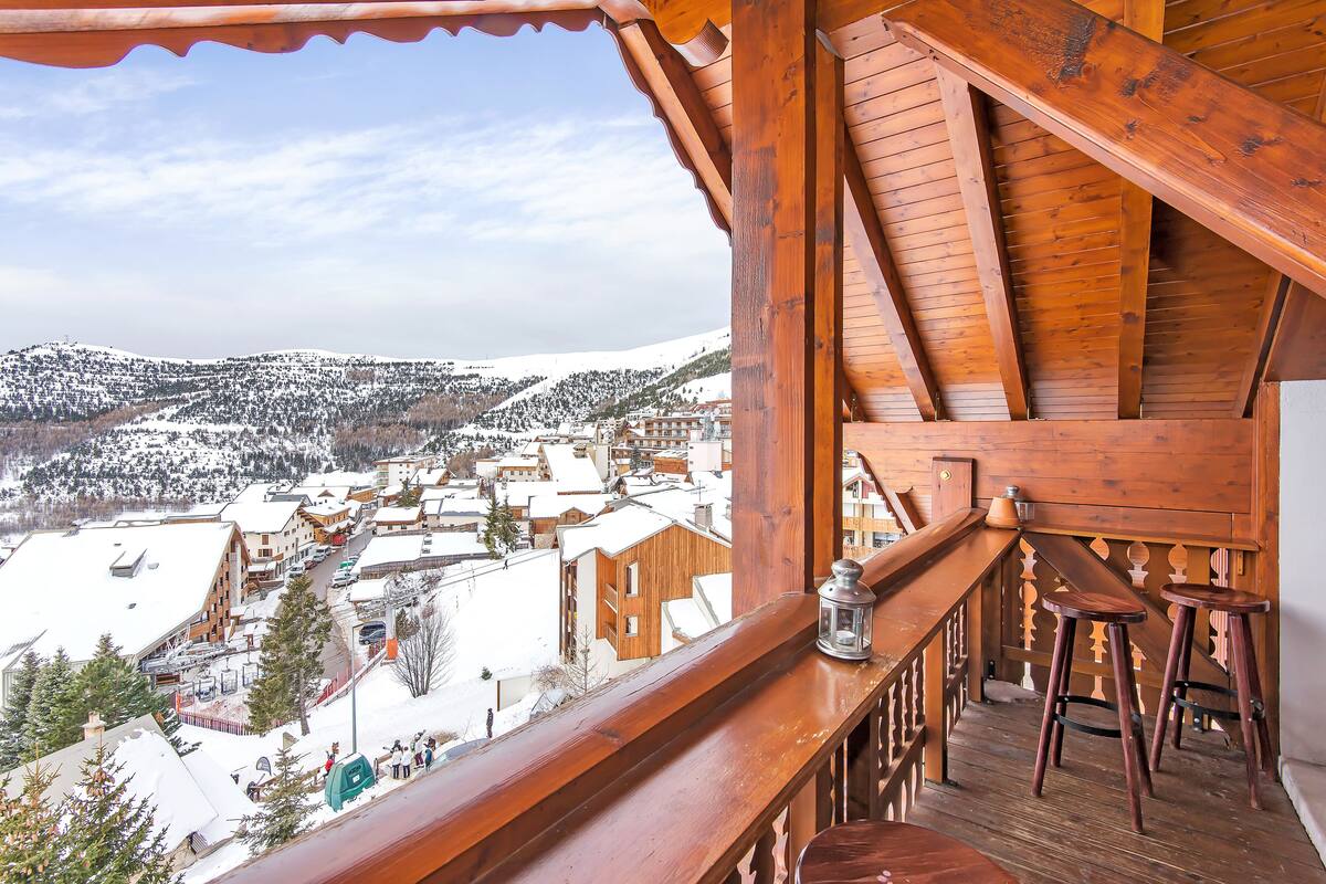 Un balcón de madera con vistas a un pueblo cubierto de nieve y montañas.