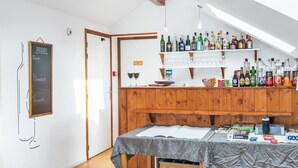 Een gezellig barretje met houten planken vol met verschillende flessen en glazen, een krijtbord met de menukaart, en een tafel met hapjes en een drankje.