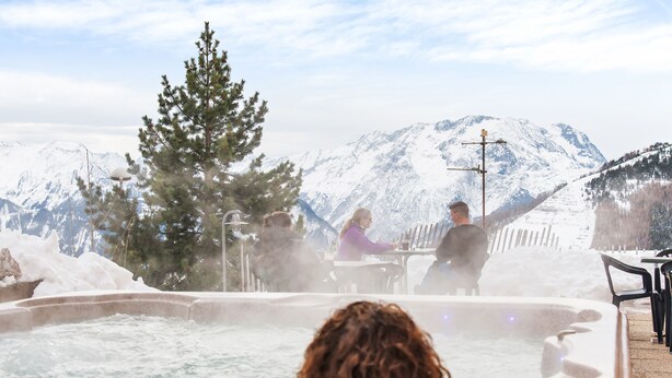 Een bubbelbad met een bergpanorama, omringd door sneeuw en bomen.