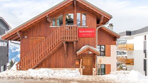 Een houten chalet met een trap, een bordje met de tekst 'Danski Belle Etoile' en uitzicht op met sneeuw bedekte bergen.