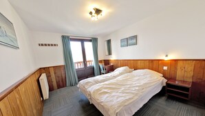 Een hotelkamer met een groot bed, houten lambrisering, een klein nachtkastje, een venster met gordijnen en een wandlamp.