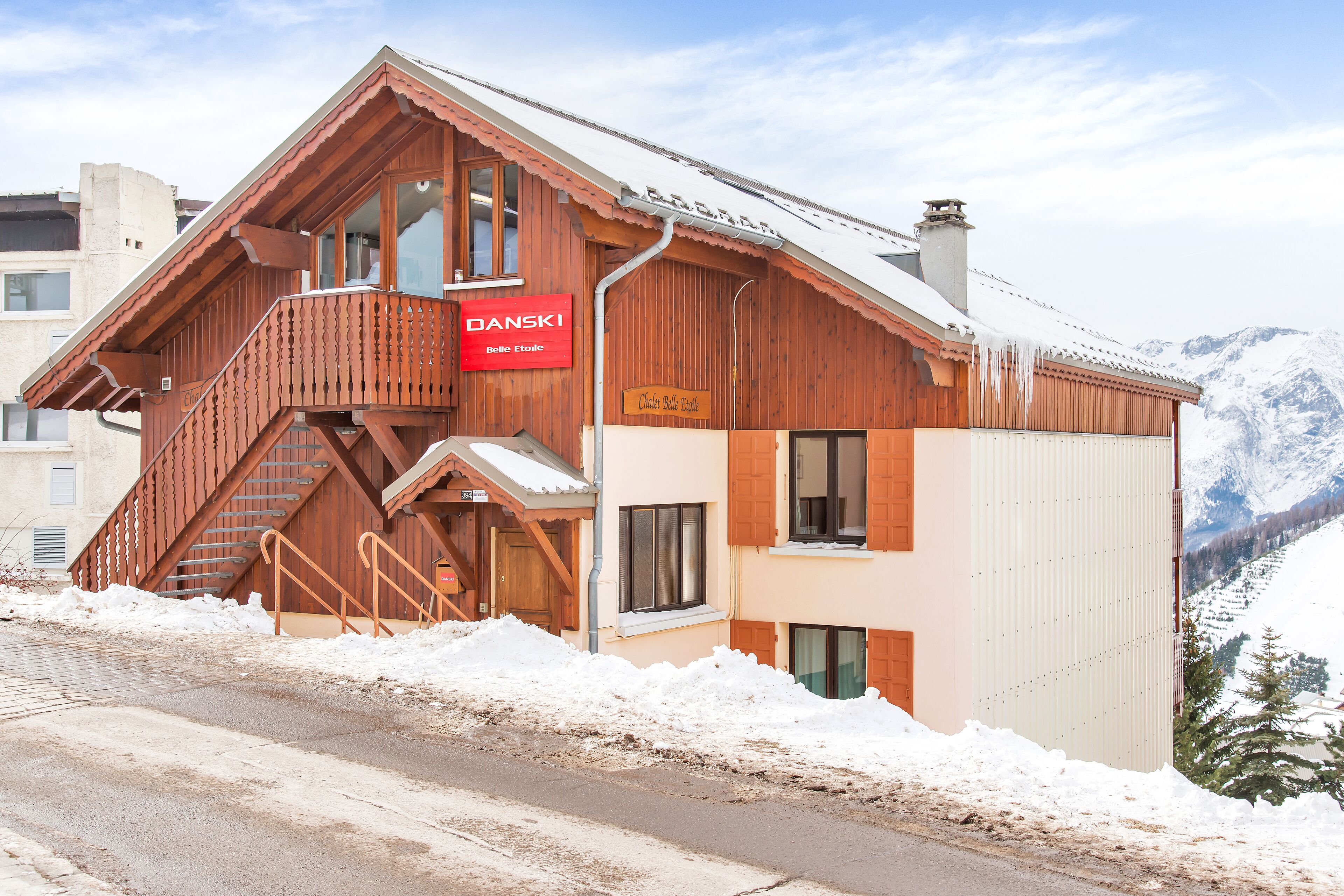 Eine Holzhütte mit rotem Schild, einer Treppe und Blick auf schneebedeckte Berge.