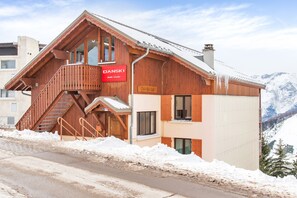 Een houten chalet met een rood bord, een trap en een uitzicht op besneeuwde bergen.