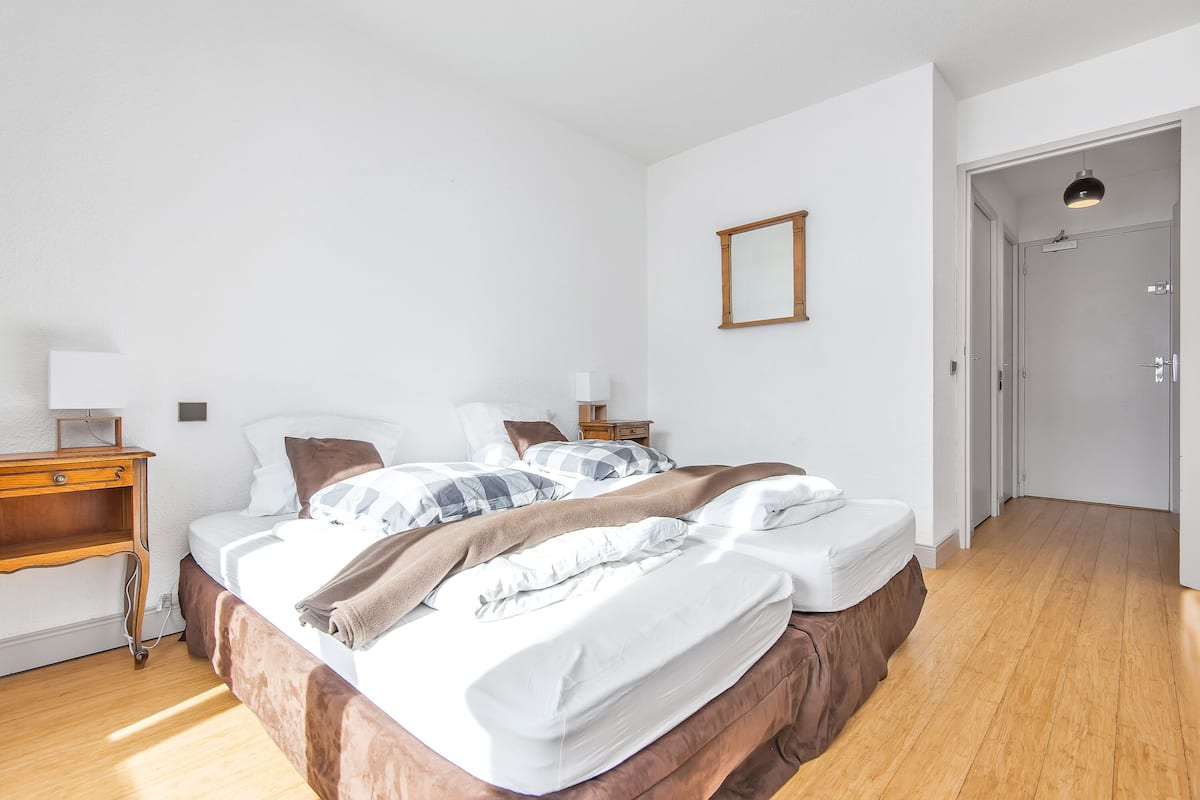 Ein Schlafzimmer mit Holzboden, einem Bett mit weißer und brauner Bettwäsche, einem Nachttisch mit Lampe und einer Tür zu einem weiteren Raum.