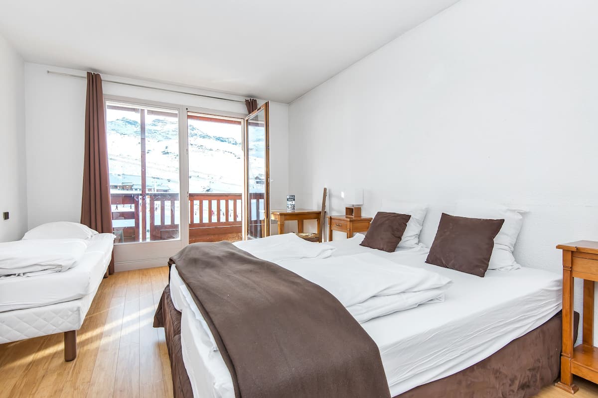 Ein Hotelzimmer mit zwei Betten, Holzboden, einem Schreibtisch und Blick auf einen verschneiten Berg.