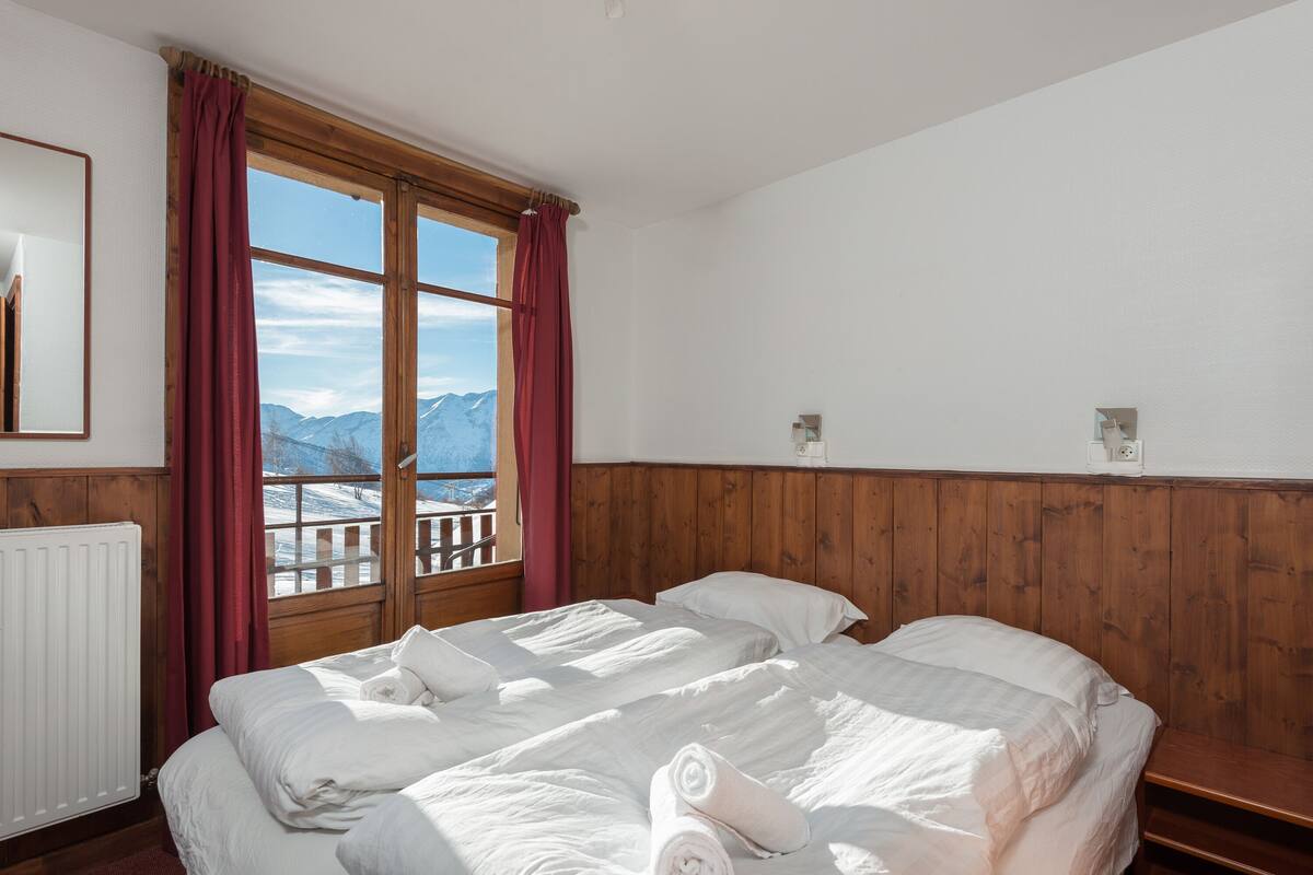 Ein Zimmer mit zwei Betten, Holzvertäfelung, einem Fenster mit Bergblick und einer Heizung.