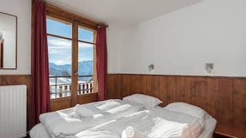 Une chambre avec deux lits, des lambris en bois, une fenêtre donnant sur les montagnes et un radiateur.