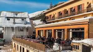 A snow-covered building with outdoor seating and a wooden deck. - Klubhotel Le Refuge by Skinetworks (Huez)