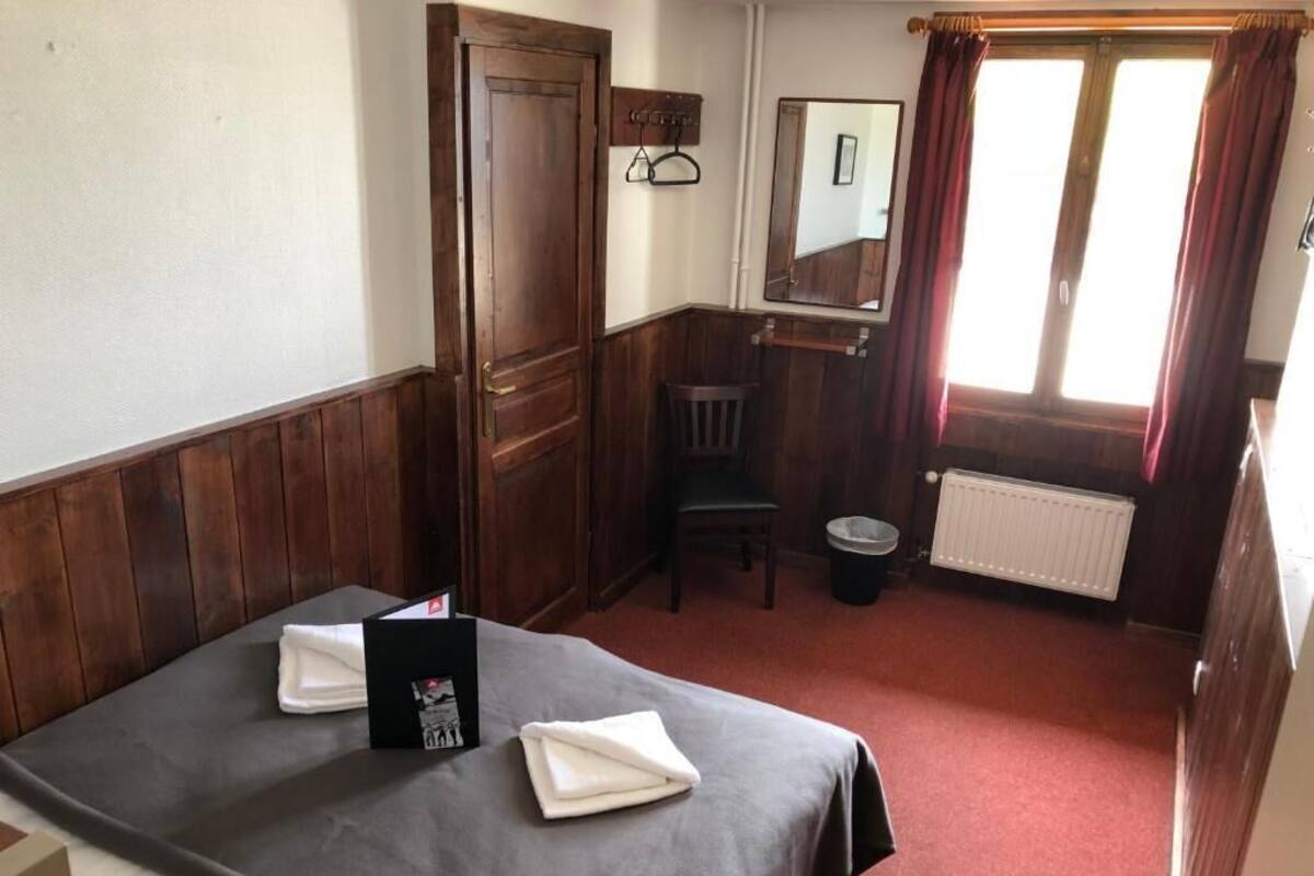 Ein Hotelzimmer mit Bett, Sessel, Heizkörper und einem fenster mit Vorhängen.