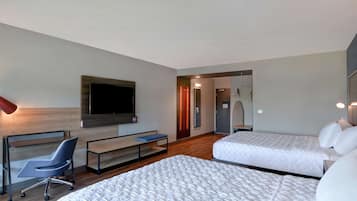 Ein modernes Hotelzimmer mit zwei Betten, einem Schreibtisch, einem Sessel, einem Fernseher und einer Dusche.