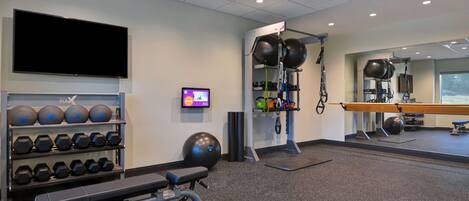 A gym with weightlifting equipment, a television, and a mirror.