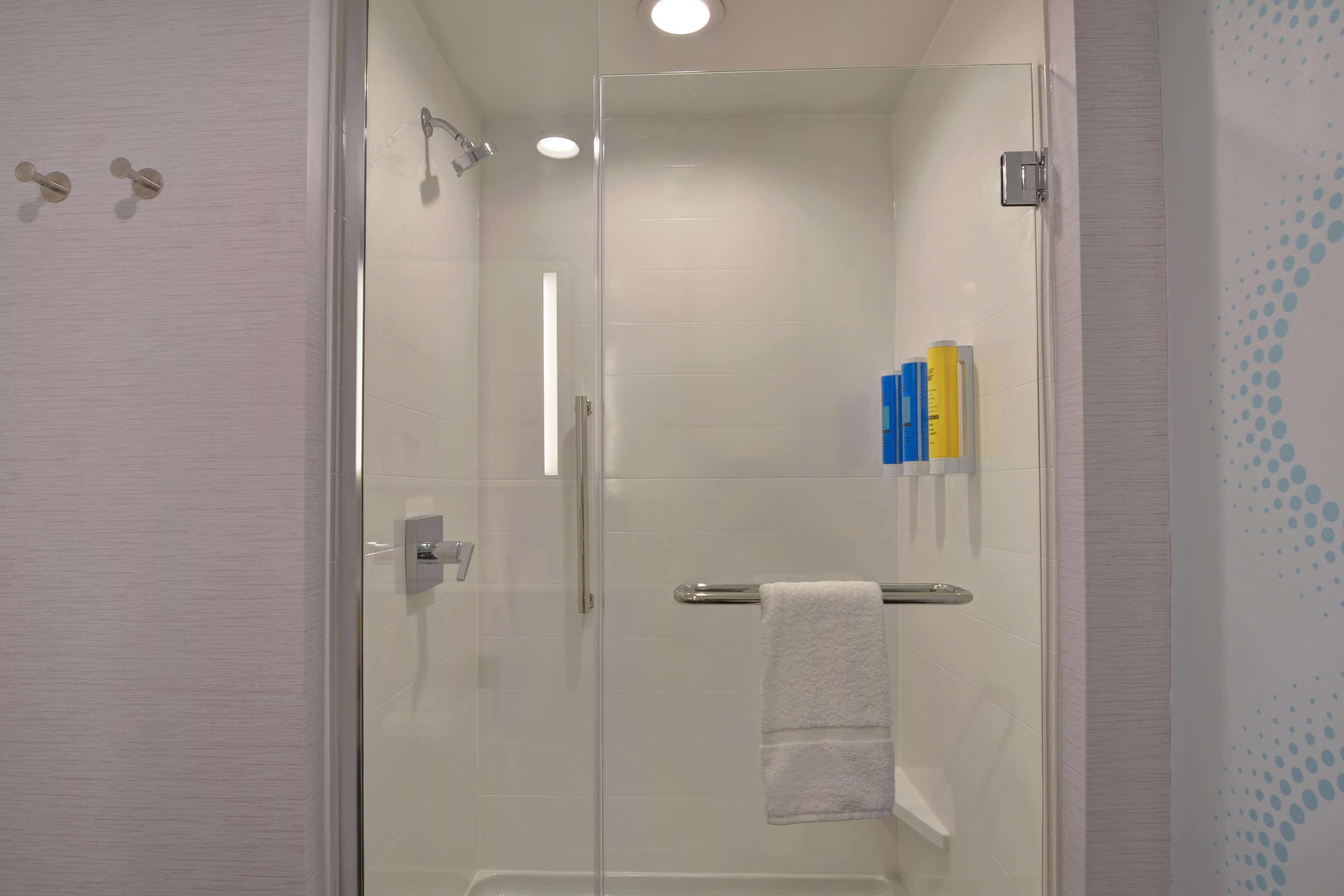 A modern bathroom with a glass-enclosed shower, a towel rack, and a shelf with toiletries.