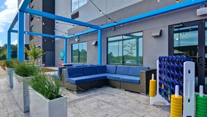 Ein Außenbereich mit Sitzgelegenheiten, einer blauen Couch, Pflanzgefäßen mit Gras und einer blau-weißen Struktur.
