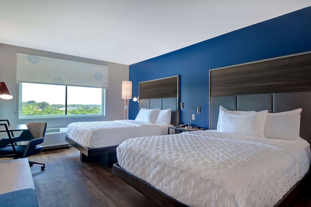 A hotel room with two beds, a desk, a chair, and a large window with a view.