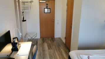 Ett hotellrum med ett skrivbord, en stol, en säng och en dörr med en skylt.