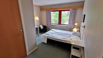 A bedroom with a bed, bedside table, chair, lamp, window, and radiator.