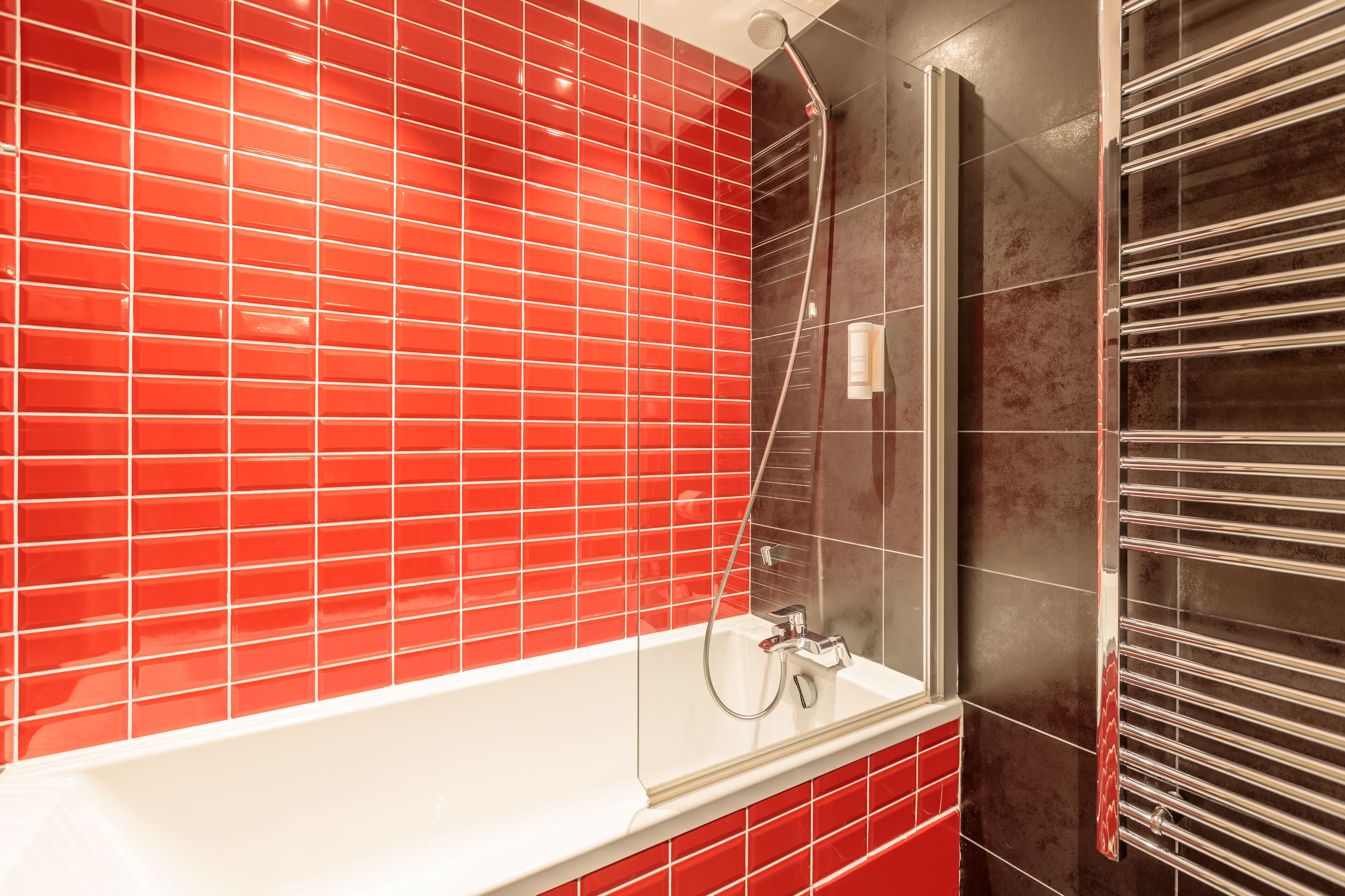 Un baño con una bañera blanca, paredes de azulejos rojos y una zona de ducha con mampara de cristal.