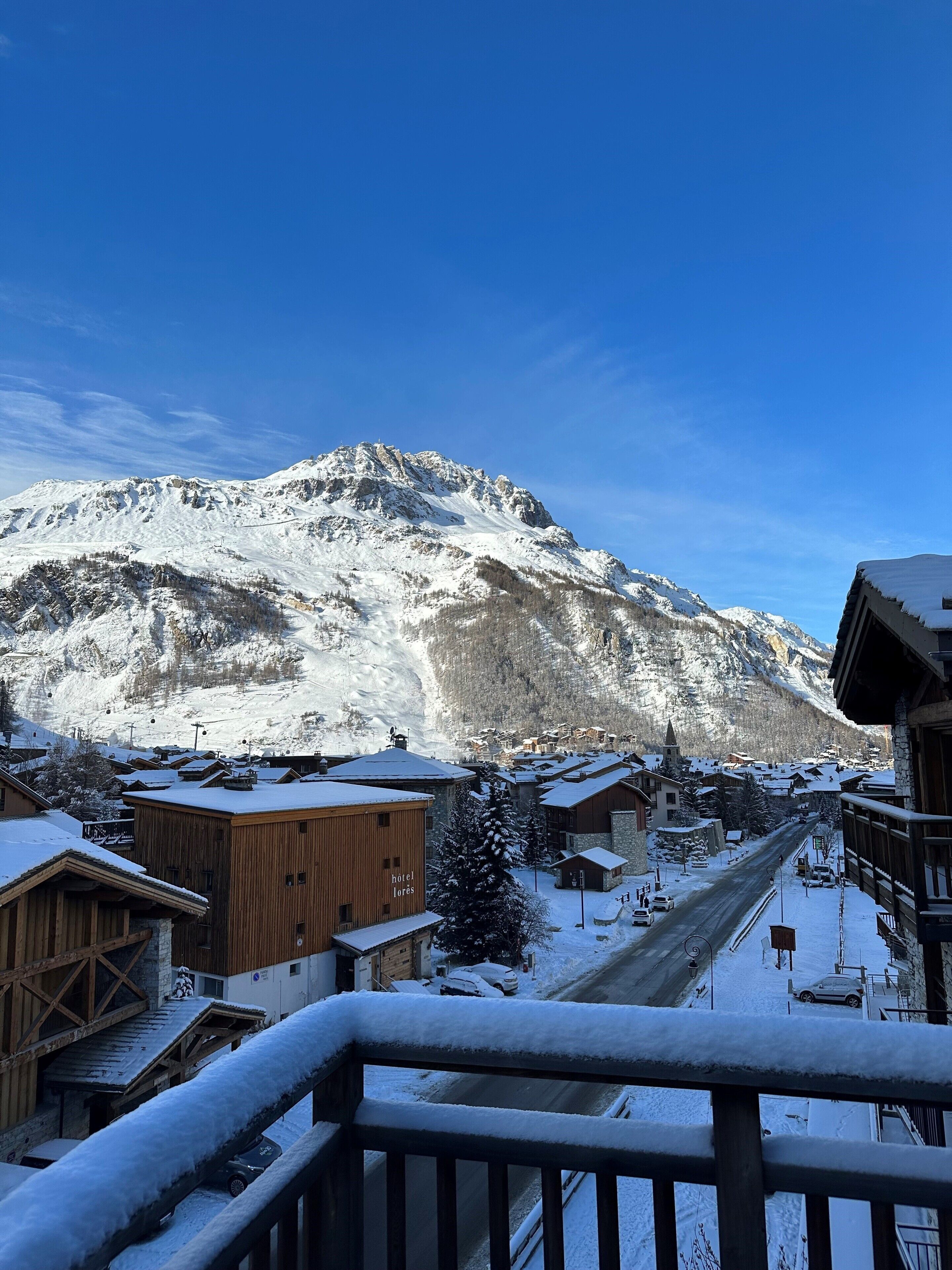 A snow-covered mountain with a ski resort in the foreground, featuring wooden buildings and a clear sky.