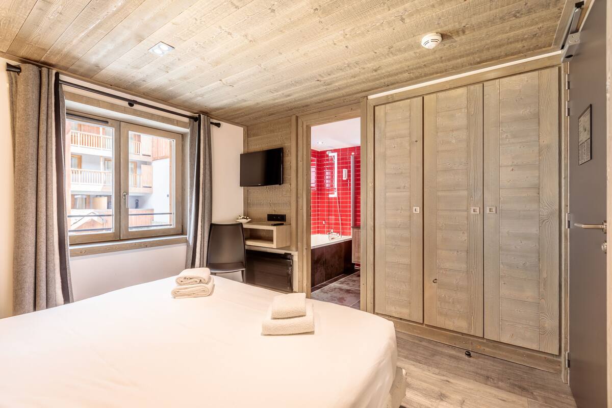 A bedroom with a large bed, a TV mounted on the wall, and a wardrobe.