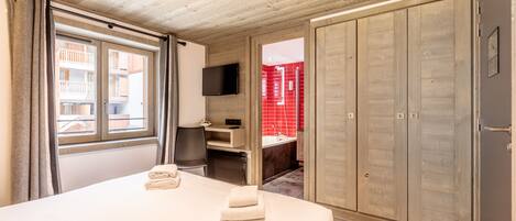Een slaapkamer met een groot bed, een tv aan de muur en een kledingkast.