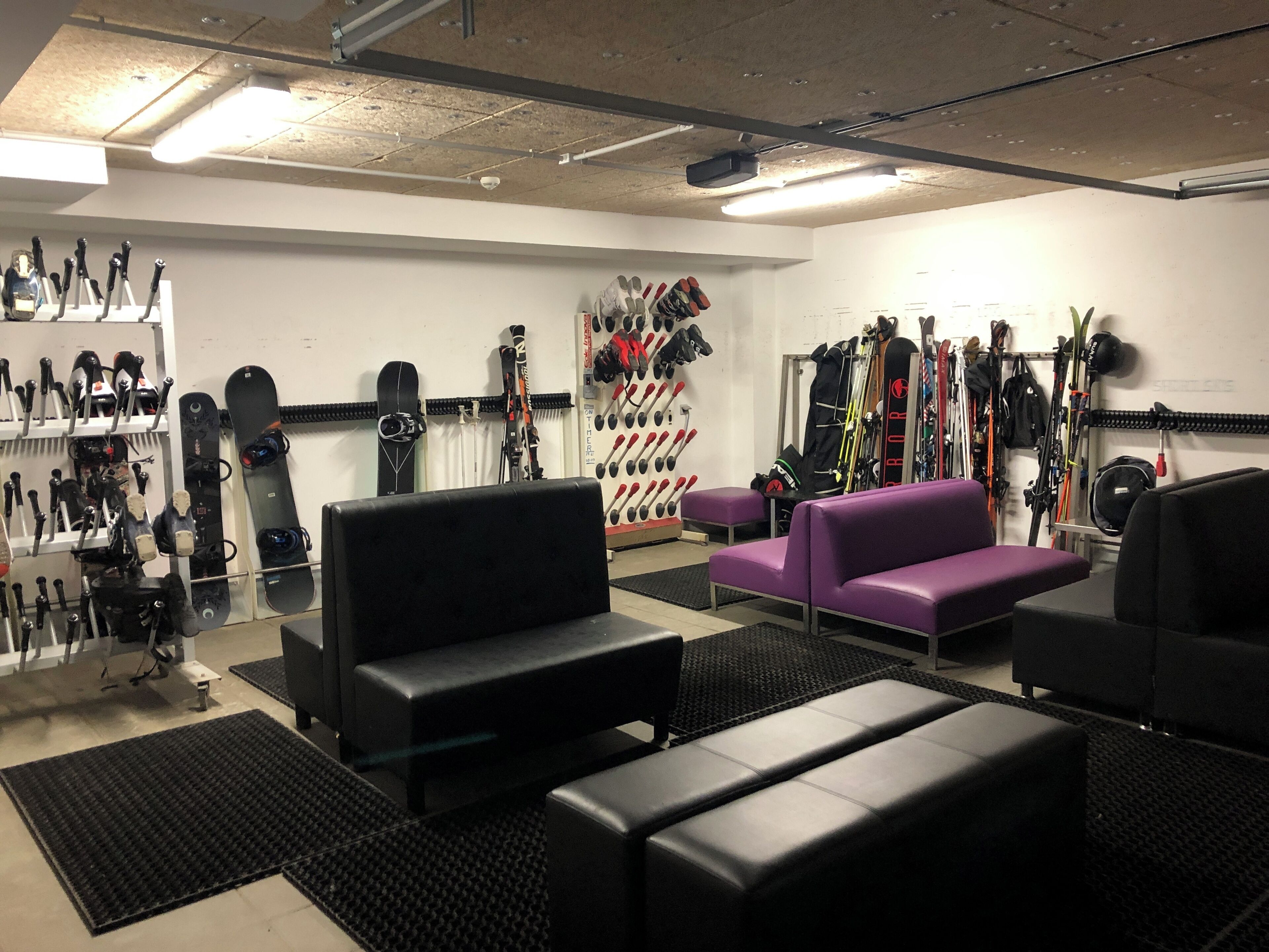 Un magasin de location de matériel de ski équipé de bancs, d'un canapé violet et proposant divers types de skis et de snowboards.