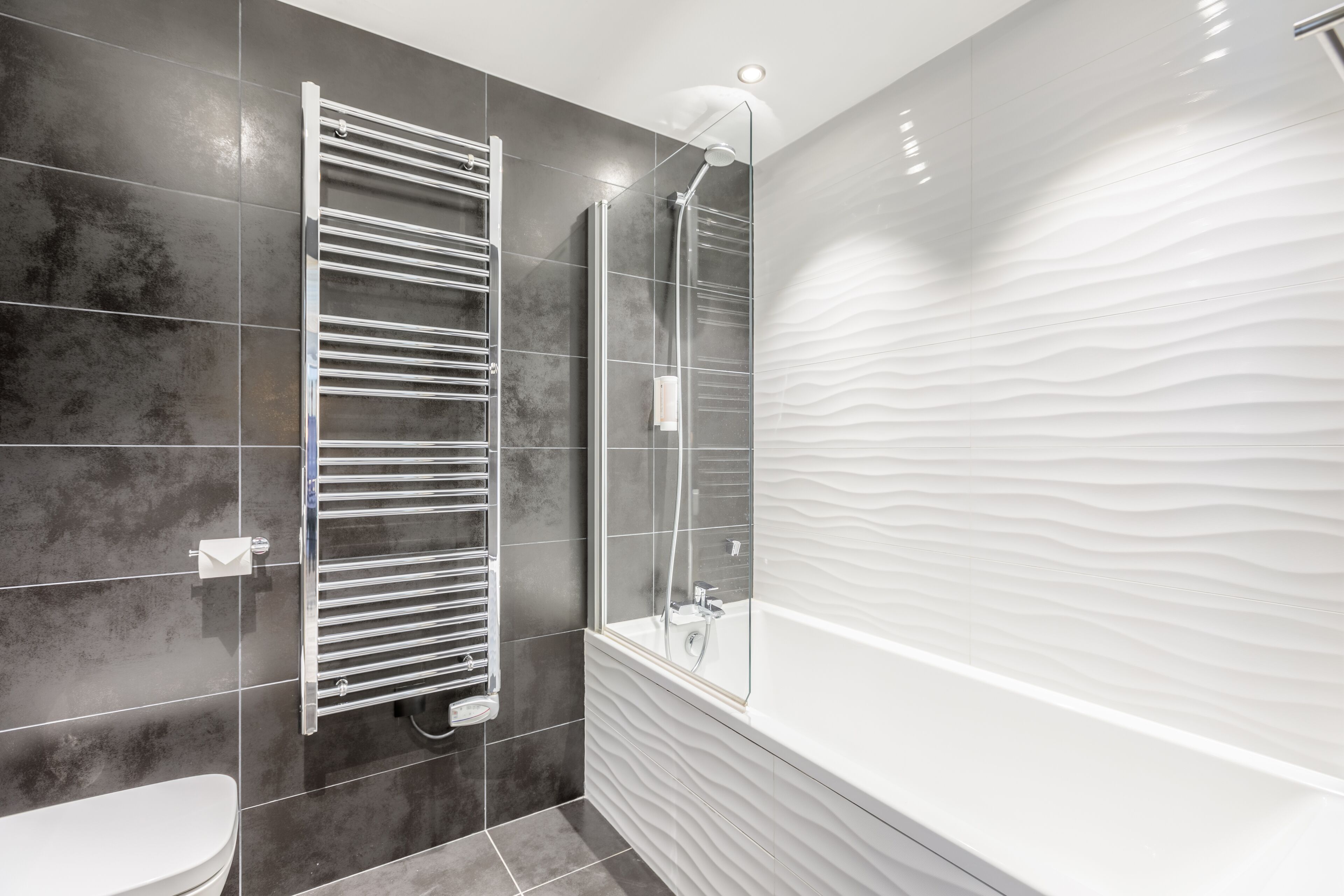 A modern bathroom with a glass shower enclosure, a white bathtub, and a towel rack.