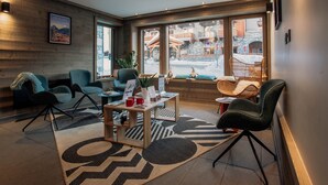 A modern hotel lobby with a wooden wall, large windows, and a seating area with chairs and a coffee table.