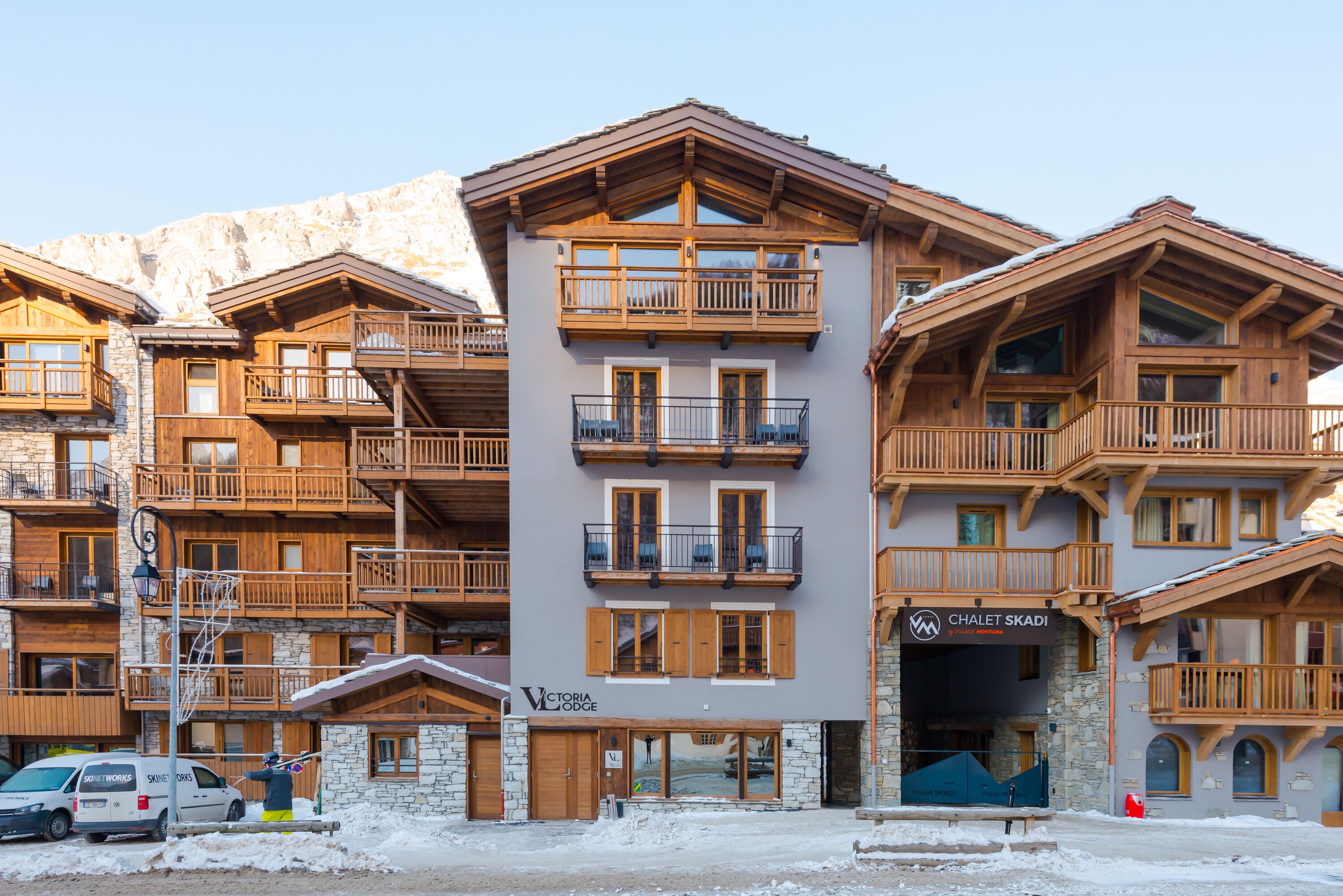 A multi-story hotel with wooden balconies and stone facade, featuring a sign for 'Chalet Skadi' and 'Victoria Lodge'.