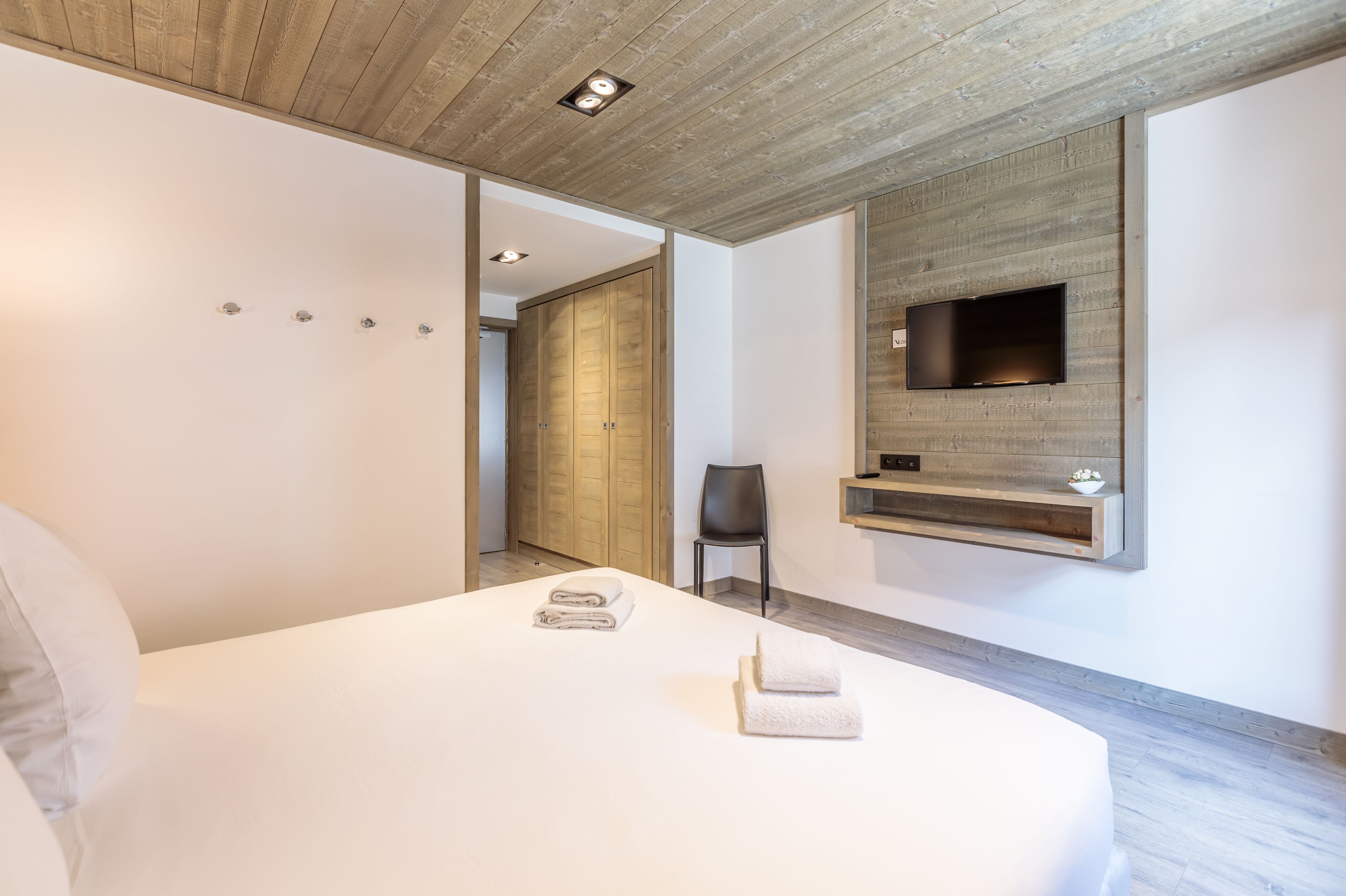 A modern bedroom with a large bed, a mounted TV, and a wooden ceiling.