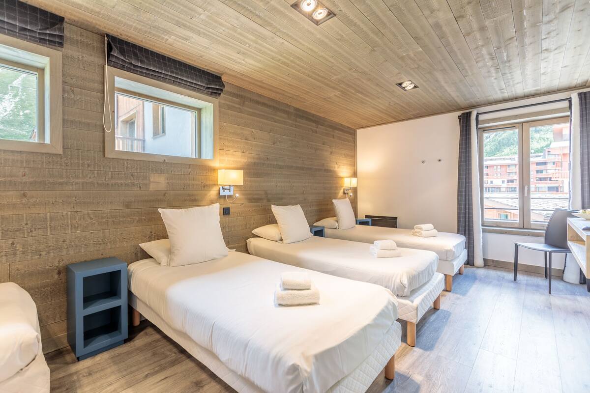 A hotel room with three beds, wooden walls, and a desk with a chair.