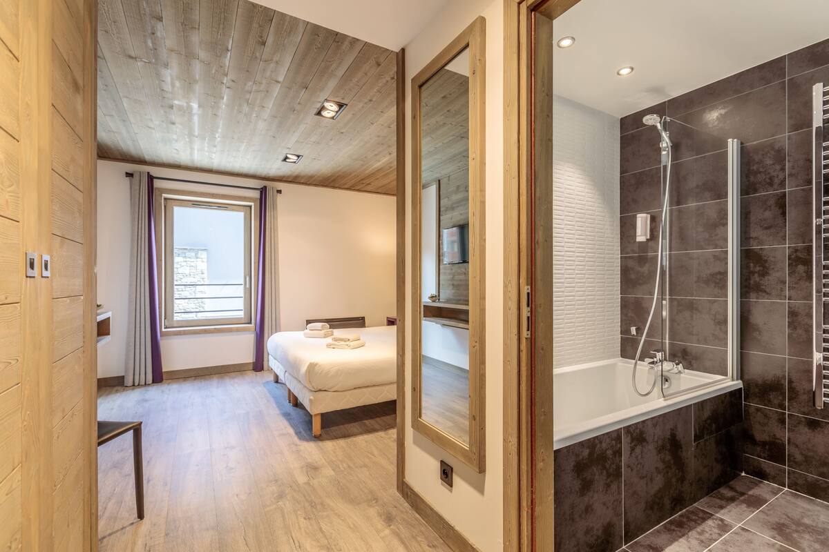 A modern hotel room with a wooden ceiling, a large bed, a walk-in shower, and a large mirror.