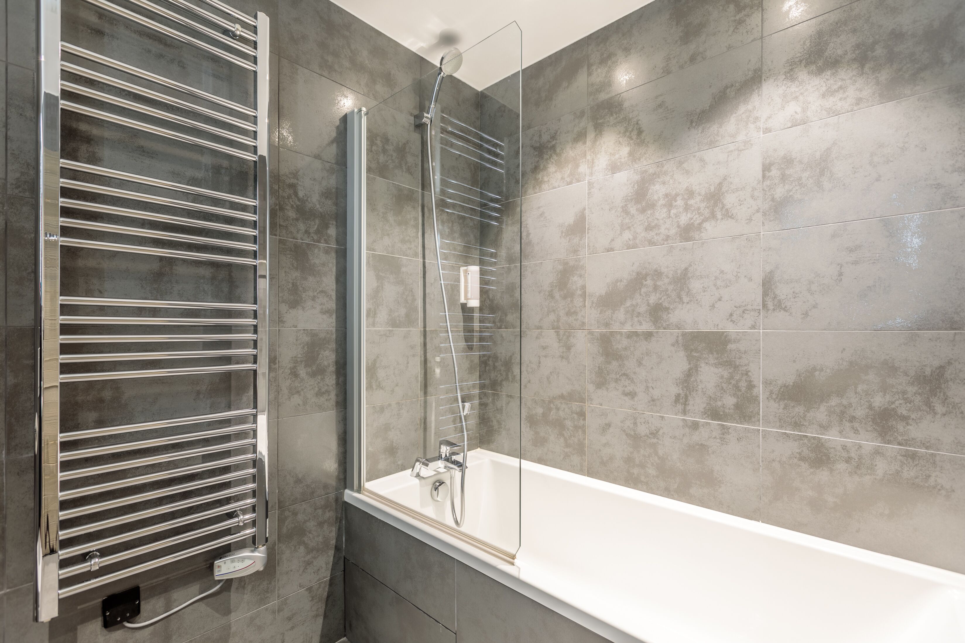 A modern bathroom with a glass-enclosed shower, a white bathtub, and a chrome towel rack.