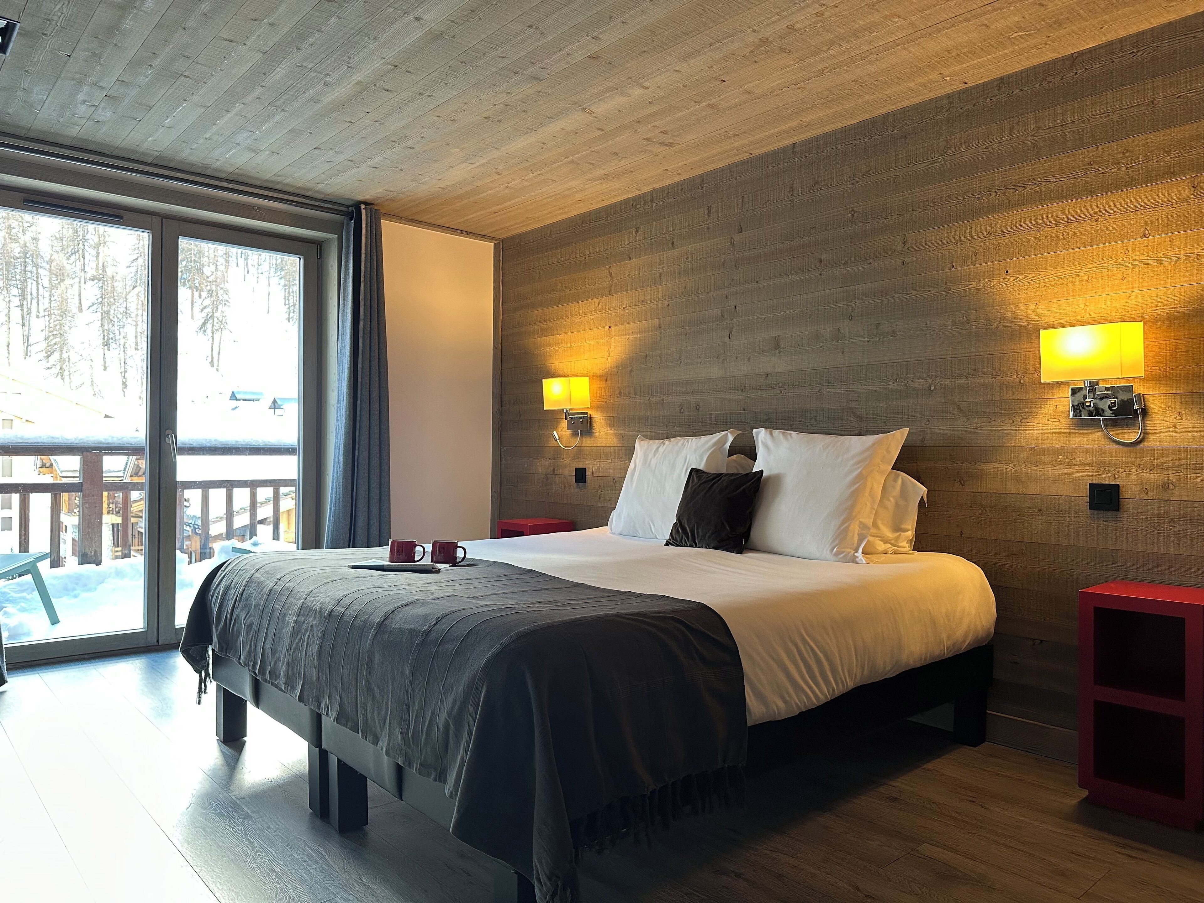 A modern bedroom with a large bed, wooden walls, and two bedside lamps.