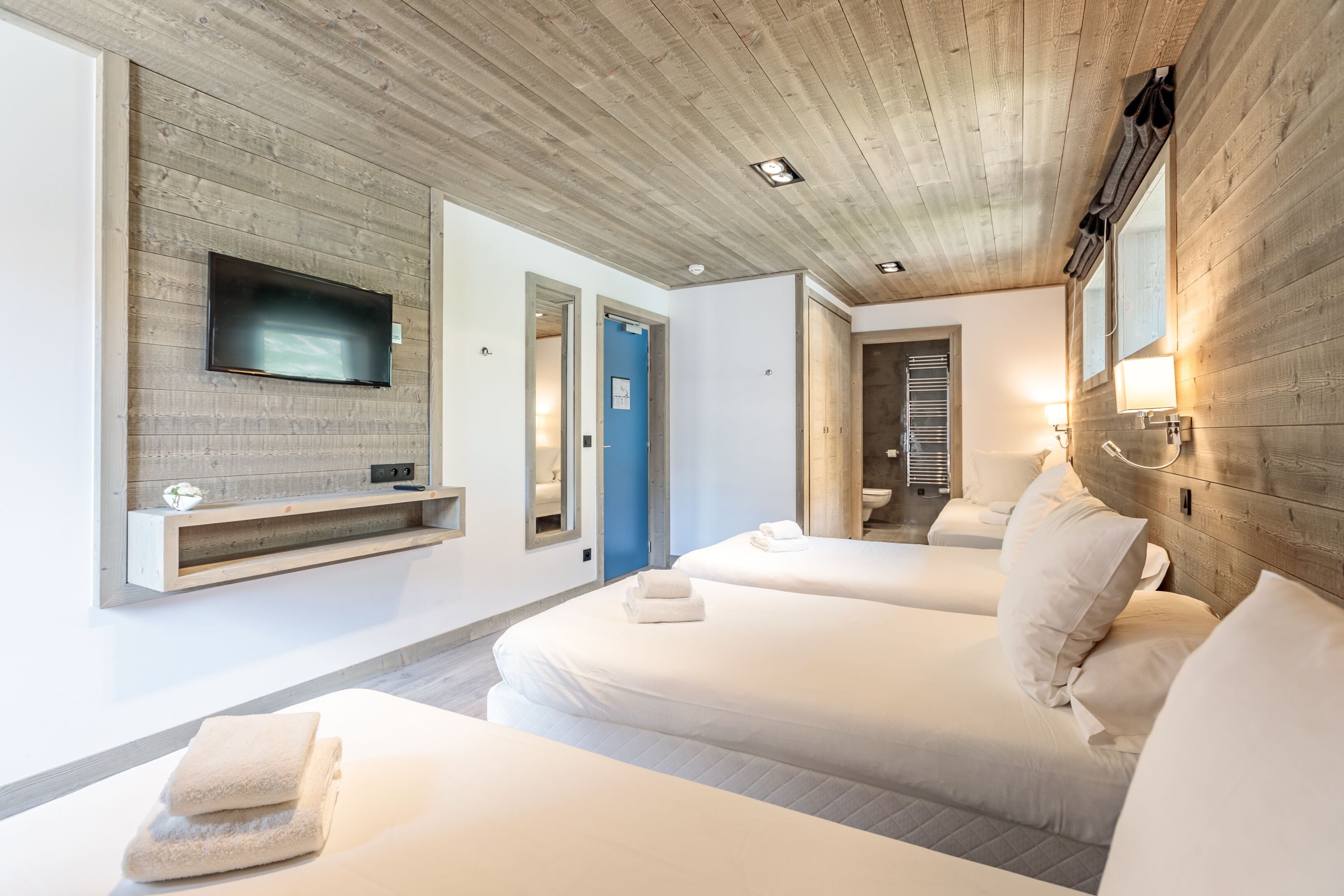 Une chambre d’hôtel moderne avec deux lits, un téléviseur fixé au mur et un plafond en bois.