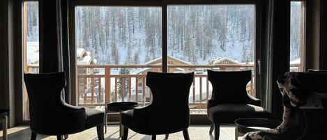 Une pièce avec trois fauteuils sombres placés face à de grandes fenêtres donnant sur un paysage enneigé parsemé de bâtiments.