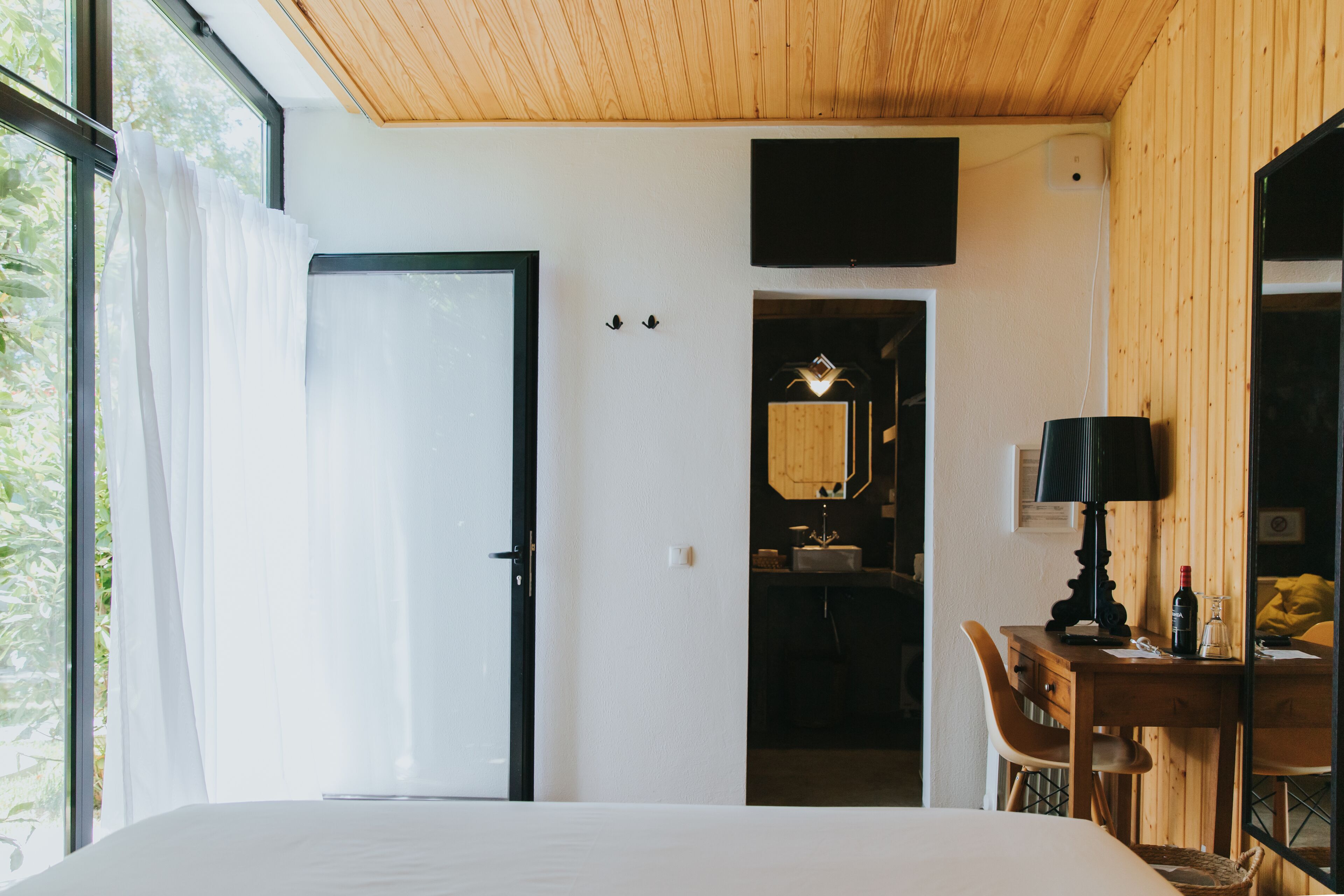 A hotel room with a bed, a desk with a lamp, a television, and a bathroom visible through an open door.
