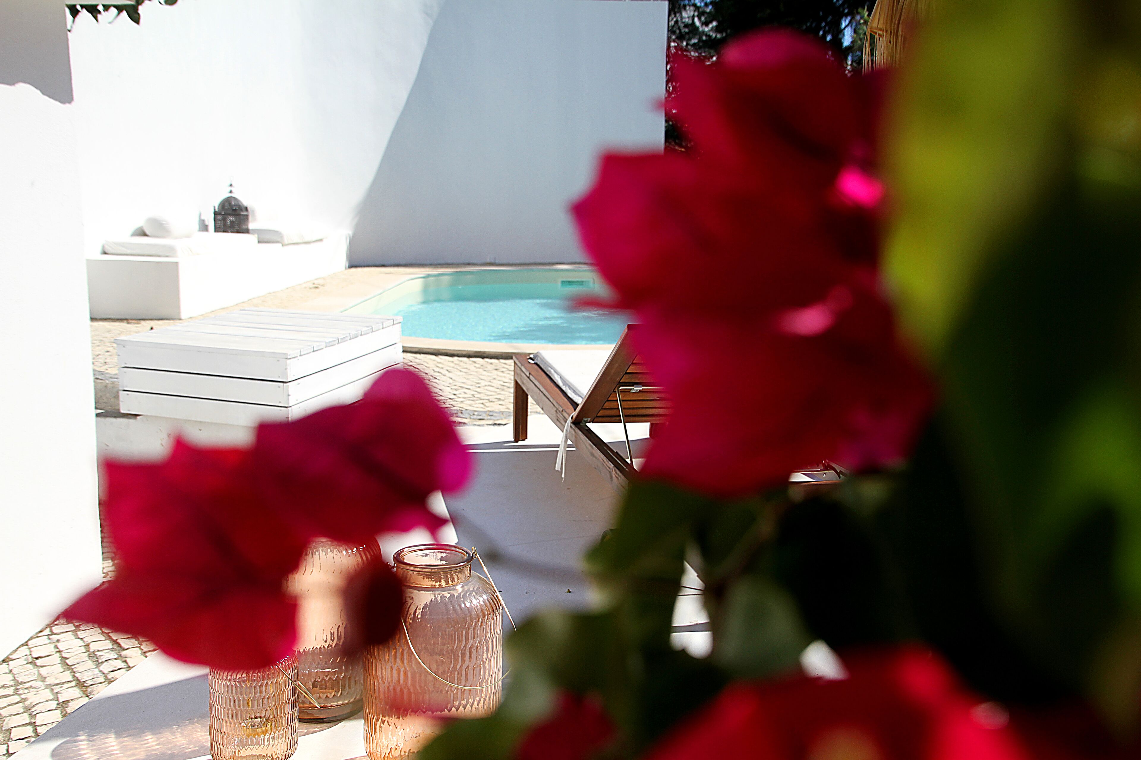 Un área de piscina con una estructura blanca, una silla de descanso y dos recipientes de vidrio.